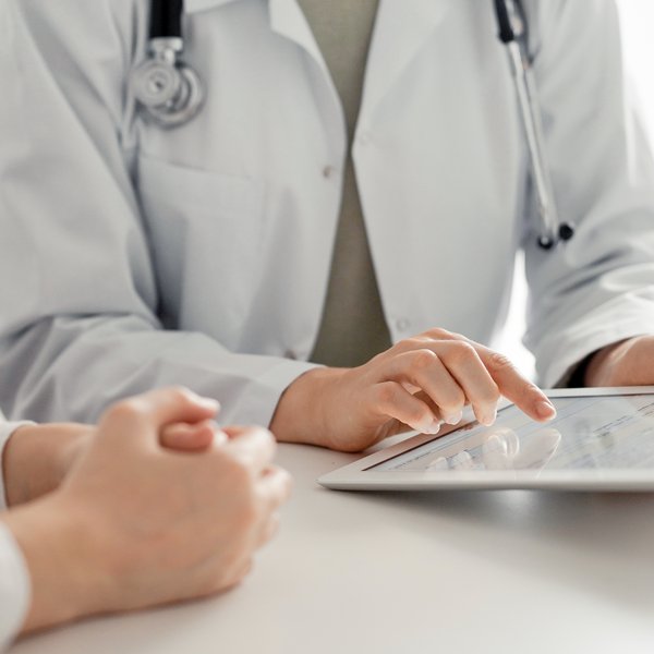 Arzt und Patient sitzen im Behandlungszimmer. Arzt hat Tablet in der Hand.