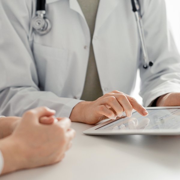 Arzt und Patient sitzen im Behandlungszimmer. Arzt hat Tablet in der Hand.